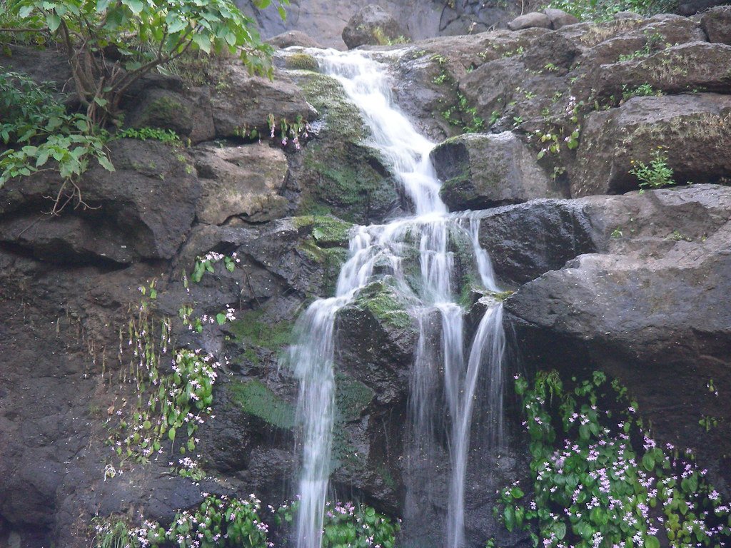 Multiple waterfalls cascading down the misty cliffs of Malshej Ghat during monsoon, surrounded by lush greenery and cloudy skies.