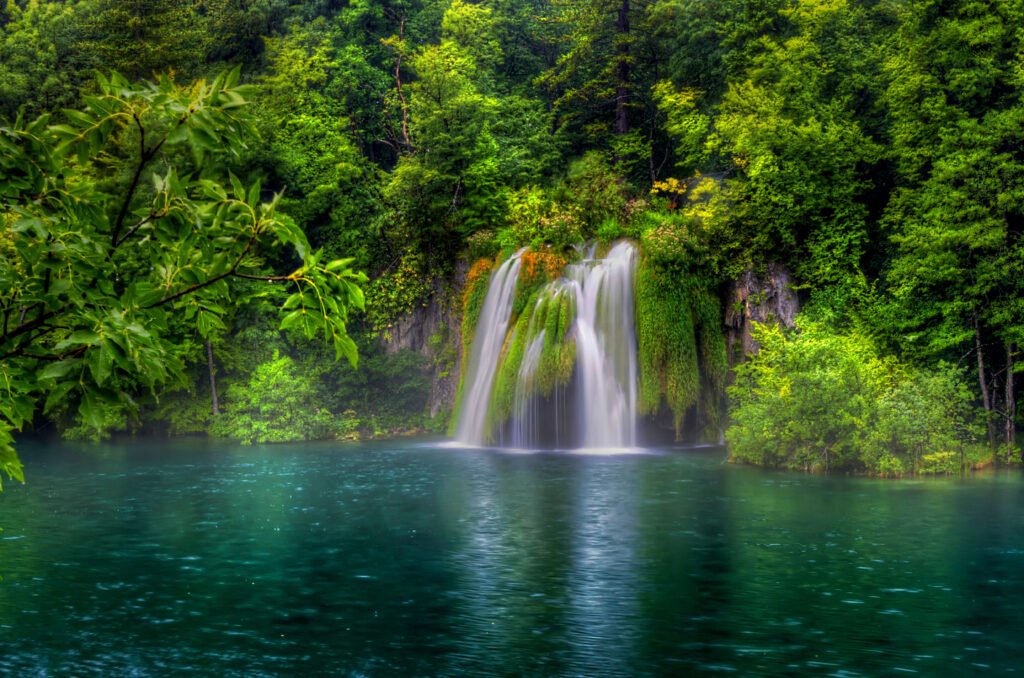 Scenic waterfall surrounded by dense green forest and crystal-clear blue water during monsoon season