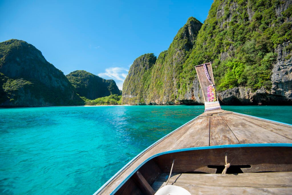 Scenic view of a tropical beach in Thailand with clear blue water, white sand, and palm trees under a sunny sky.